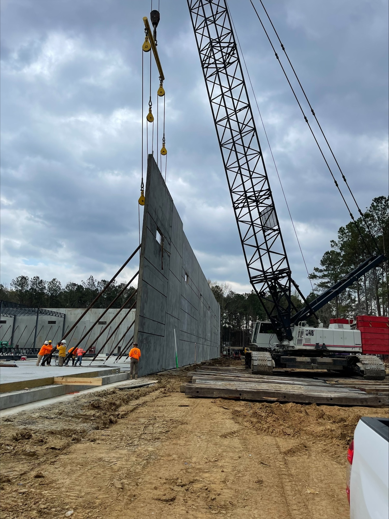 Crane lifting a tilt-up concrete wall panel while crew members guide it